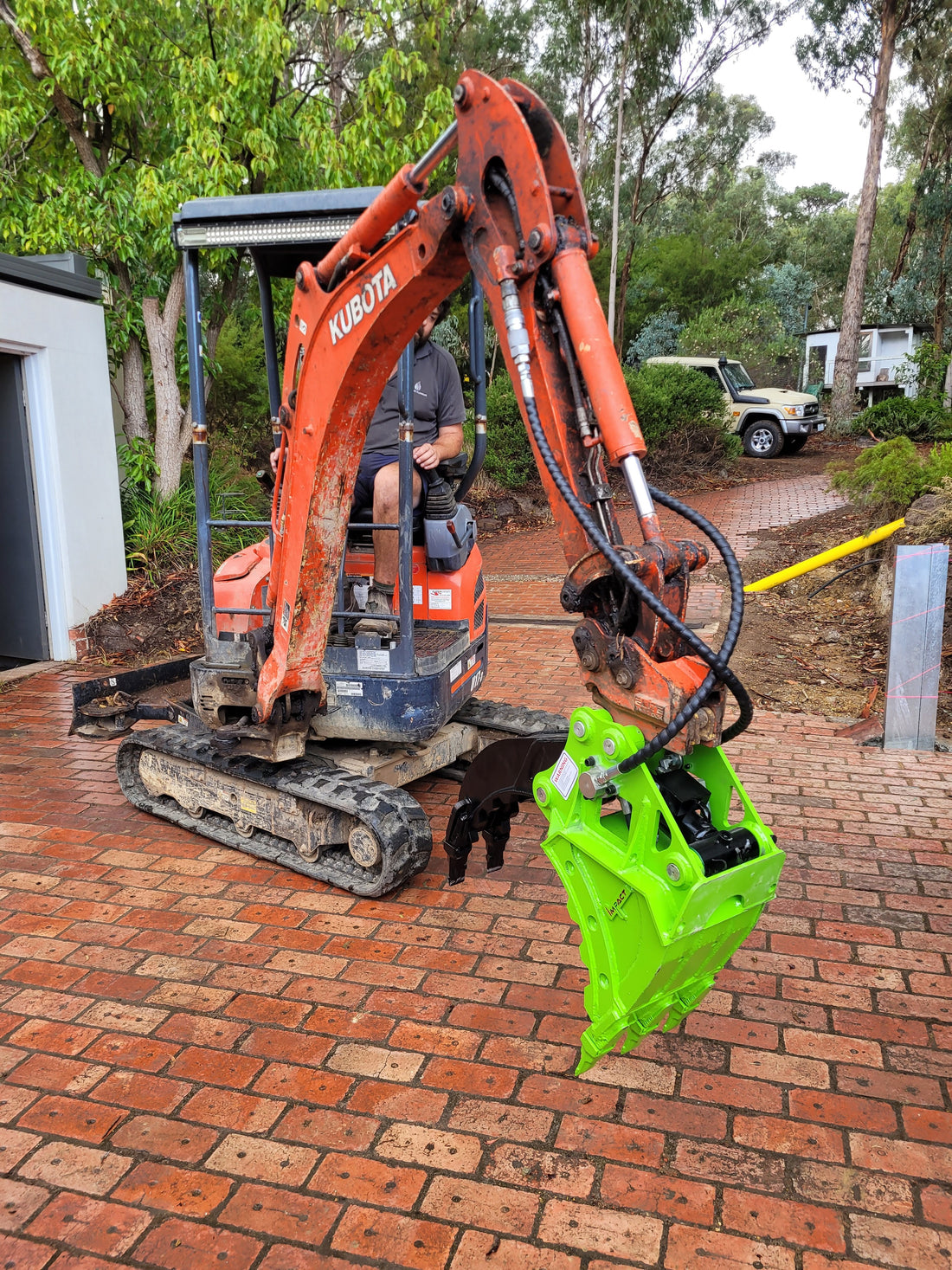 This image captures a Kubota mini excavator equipped with an Impact brand five-finger grab attachment, efficiently loading materials onto a truck bed. The five-finger grab attachment is designed for precise material handling, ideal for tasks such as landscaping, construction, and site clearing. The robust construction of both the grab and the excavator ensures durability and reliability, providing enhanced productivity for operators in various applications.