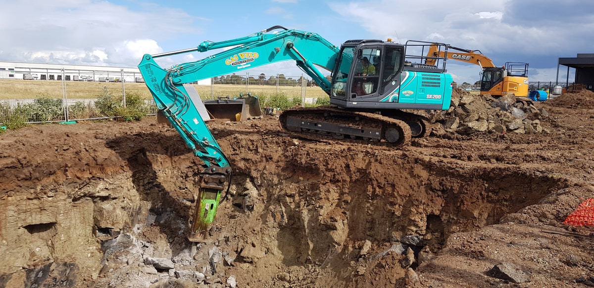 Excavator equipped with an Impact hydraulic breaker in action at a construction site, demonstrating rock breaking capabilities for excavation and site preparation