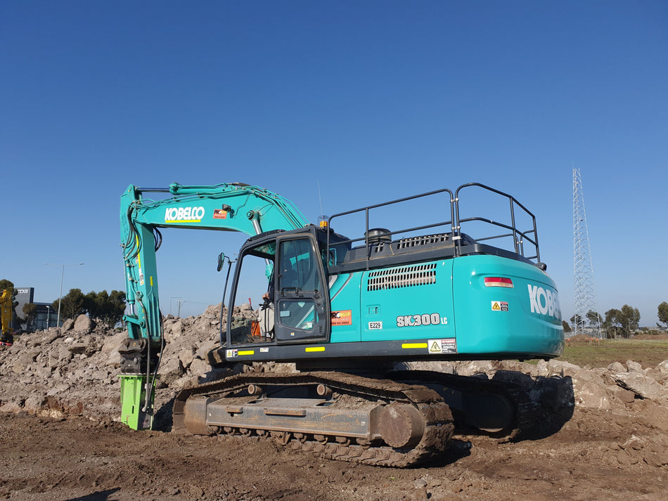 Kobelco SK300LC excavator equipped with an Impact Attachments hydraulic breaker, performing heavy-duty demolition work on a construction site
