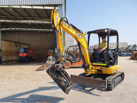 JCB mini excavator equipped with a hydraulic tilt bucket attachment, expertly maneuvered by an operator. This compact construction equipment is ideal for precision digging, grading, and landscaping tasks, offering versatile performance in tight spaces. The durable design and advanced features ensure efficient operation in various construction and earthmoving projects.