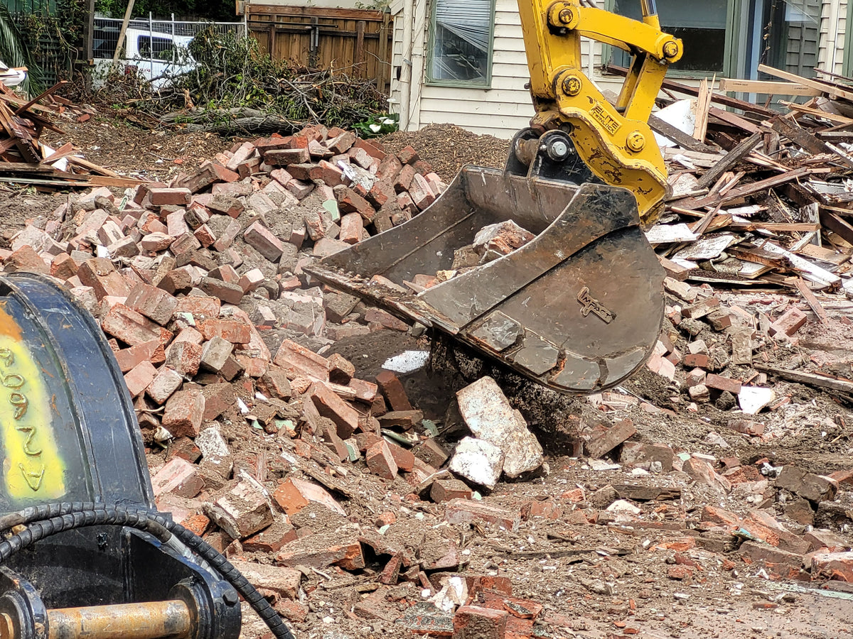 Impact Attachments excavator bucket lifting and removing brick debris during a demolition project.