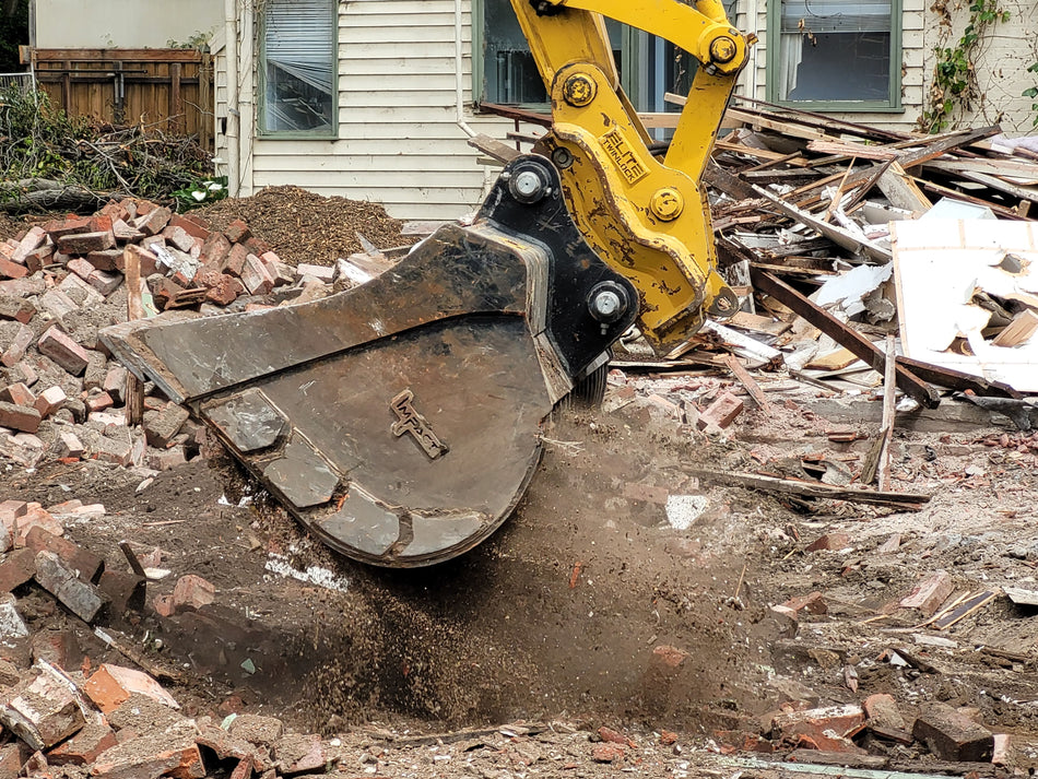 Impact Attachments excavator bucket scooping up debris and soil during a demolition and cleanup operation