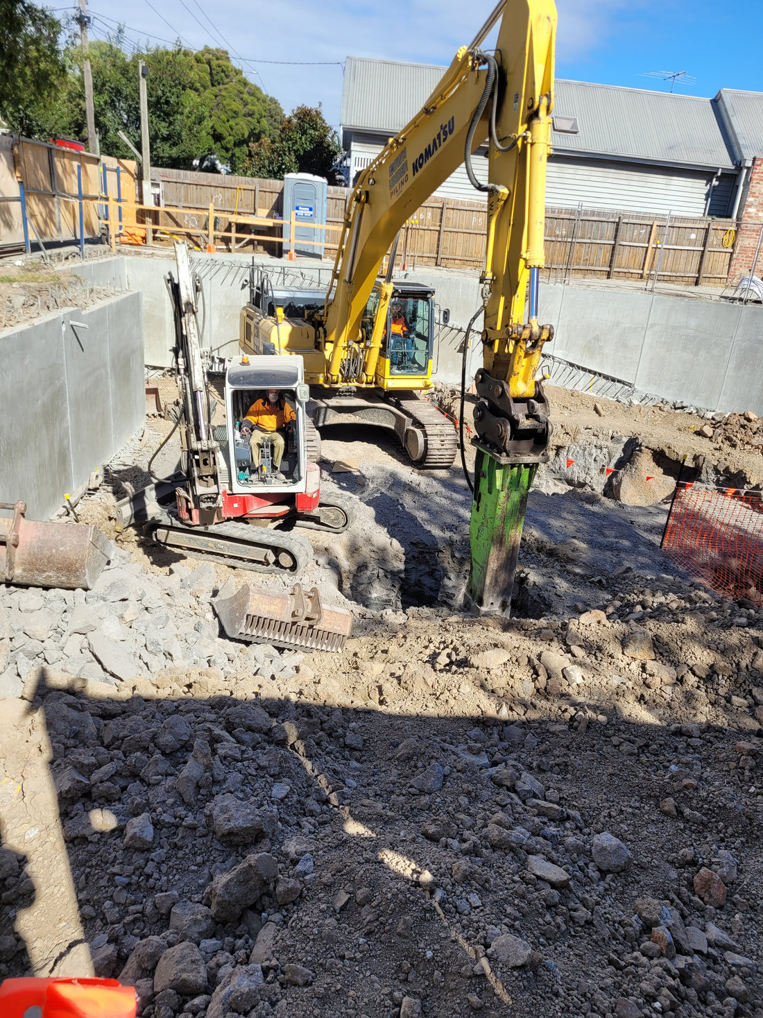Excavation site featuring a Komatsu excavator equipped with an Impact hydraulic breaker and a mini excavator, performing rock-breaking tasks in a construction zone