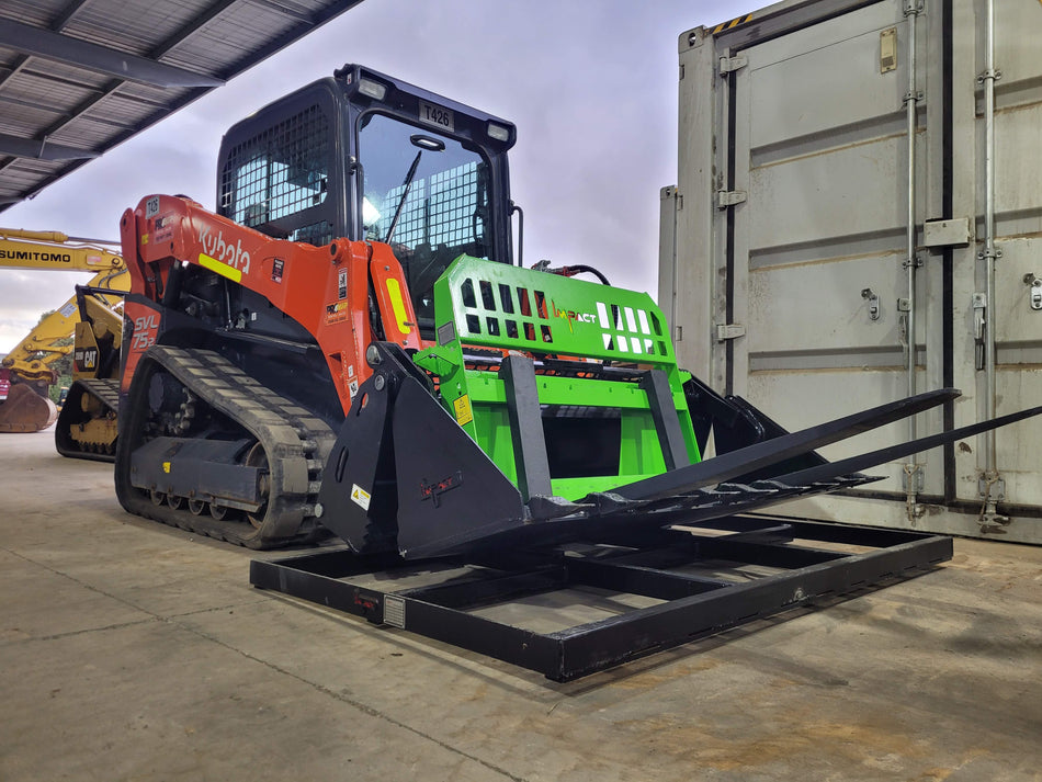 An orange Kubota SVL75-2 skid steer loader equipped with a green Impact pallet fork attachment, featuring a 4-in-1 bucket and a smudge bar, positioned on a loading dock. The loader is aligned with a pallet on the ground, ready for material handling. The scene takes place in a covered area next to a large shipping container