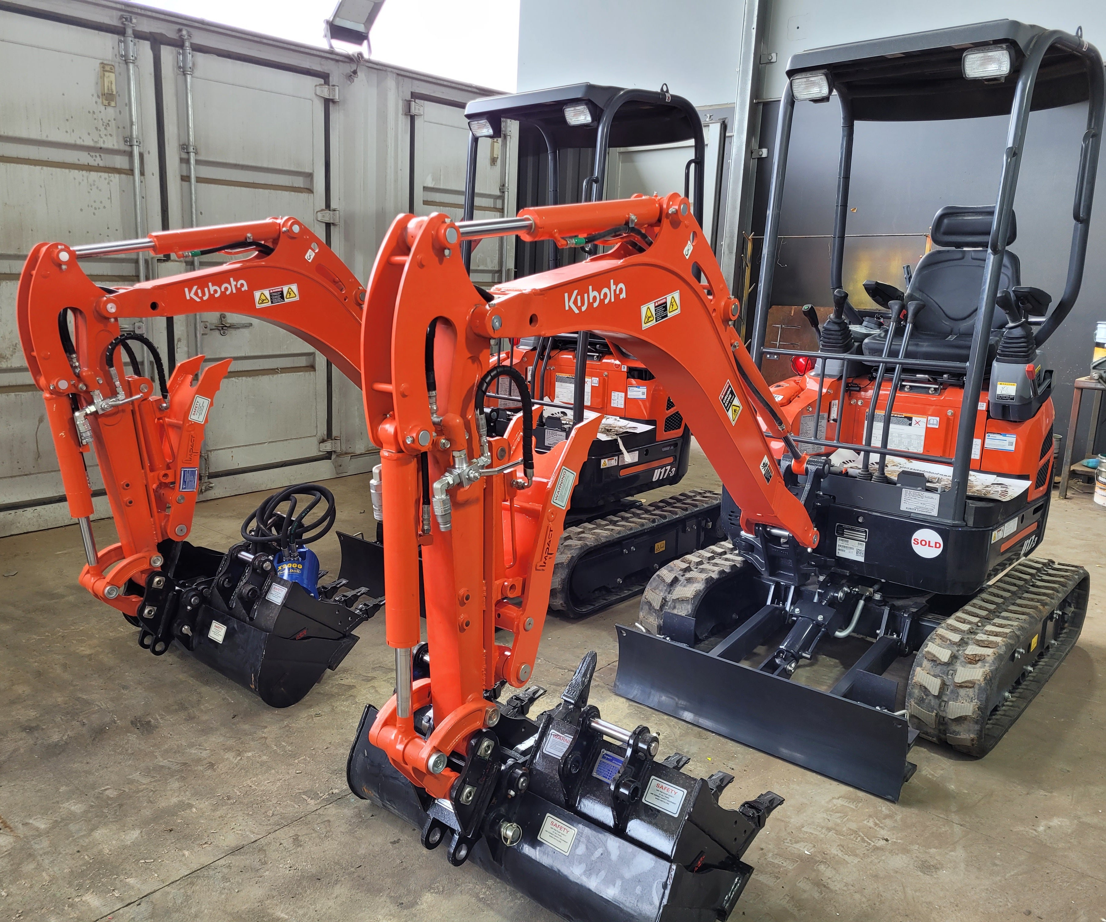 Row of Kubota mini excavators equipped with hydraulic thumbs and buckets, lined up in an industrial yard, ready for deployment in various construction, excavation, and landscaping projects. The hydraulic thumbs enhance material handling capabilities, making these machines ideal for precision work in tight spaces. Kubota mini excavators are known for their reliability, efficiency, and versatility on job sites
