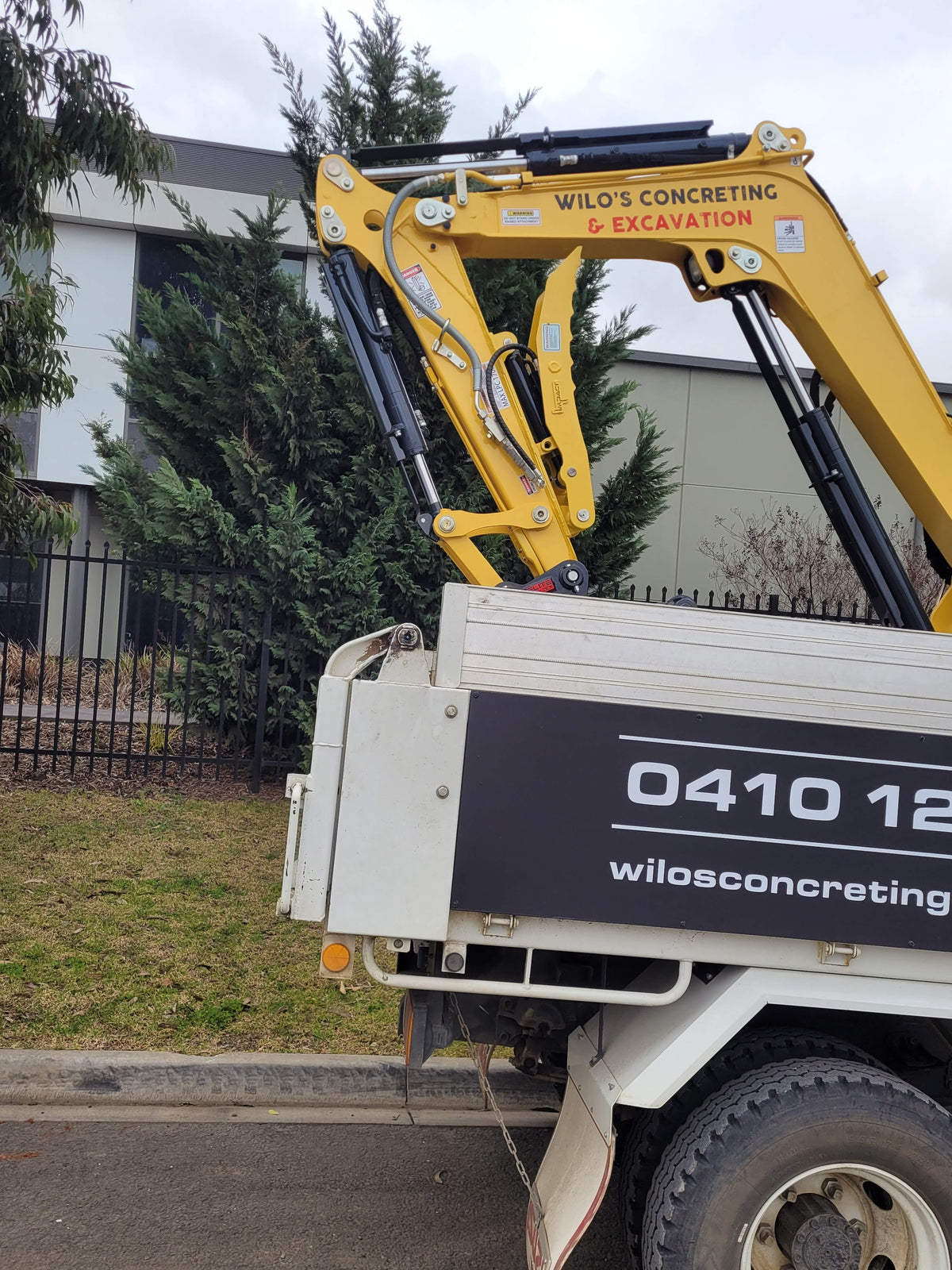 Wilo’s Concreting & Excavation truck carrying a 3-tonne excavator, showcasing professional concrete services including driveways, paving, exposed aggregate, and shed slabs, with contact details prominently displayed.