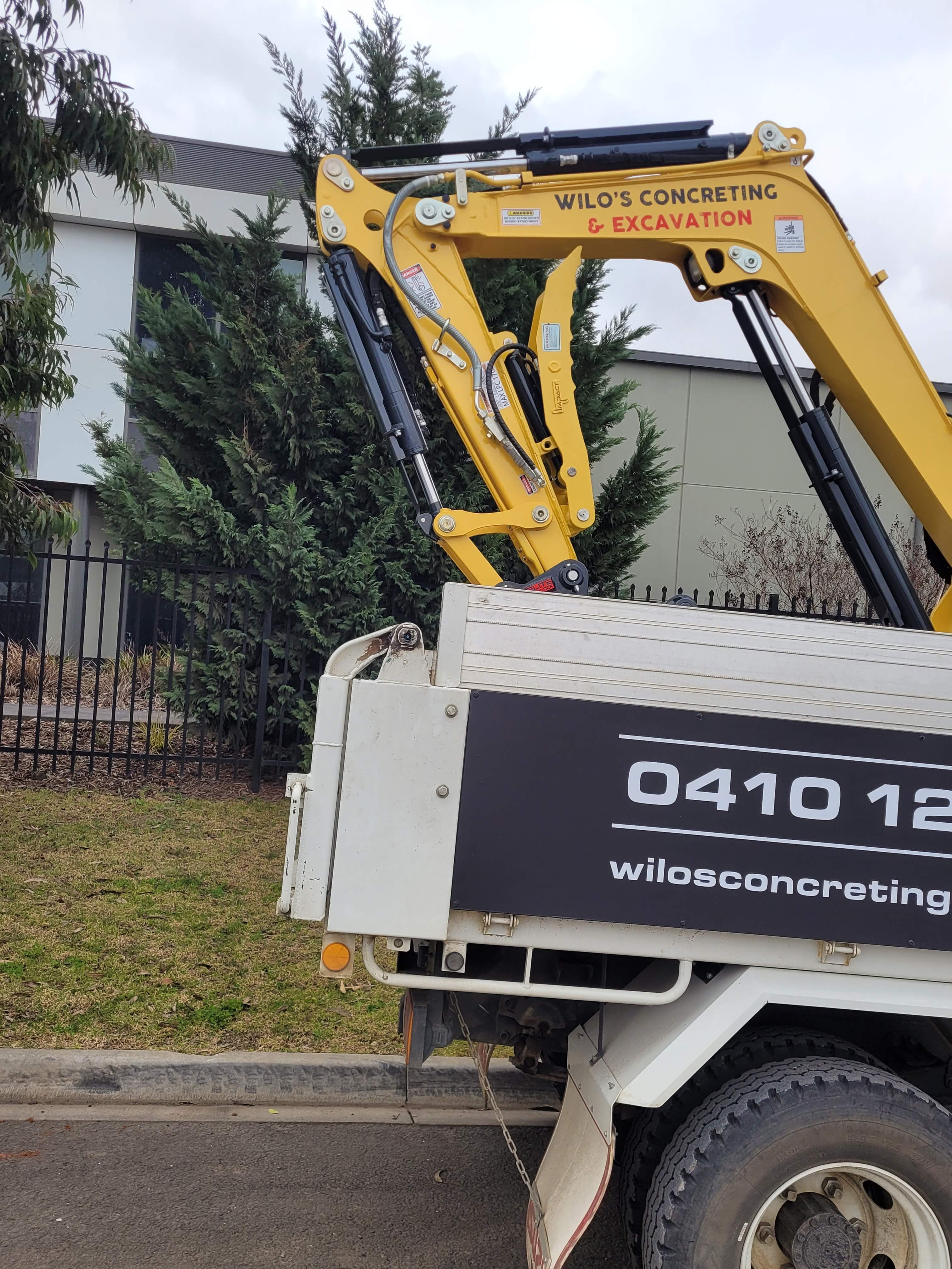 Wilo’s Concreting & Excavation truck carrying a 3-tonne excavator, showcasing professional concrete services including driveways, paving, exposed aggregate, and shed slabs, with contact details prominently displayed.