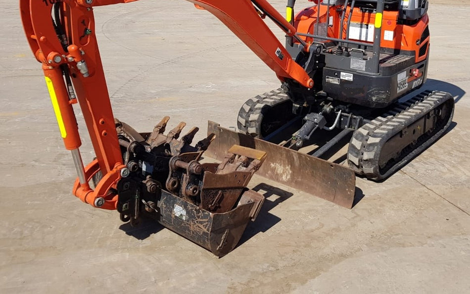 Excavator equipped with a bucket kit attachment, displayed on a concrete surface. The bucket kit includes multiple buckets of varying sizes, suitable for different digging and earthmoving tasks. The excavator's arm is extended, showcasing the versatility of the attachment. The machine is prepared for a range of construction and excavation activities.