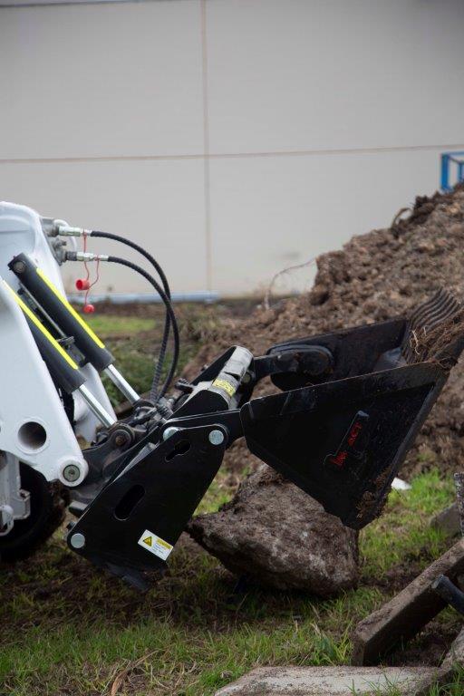 Track loader / skid steer equipped with a 4 in 1 bucket attachment, clearing brush and debris on a construction site, demonstrating versatility and power for heavy-duty tasks. Ideal for various excavation and earthmoving applications.