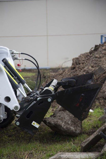 Close-up of a track loader equipped with an Impact 4 in 1 attachment, lifting a large rock on a grassy construction site. The grab attachment is ideal for handling irregularly shaped materials like rocks and debris, providing versatility in excavation and demolition projects.