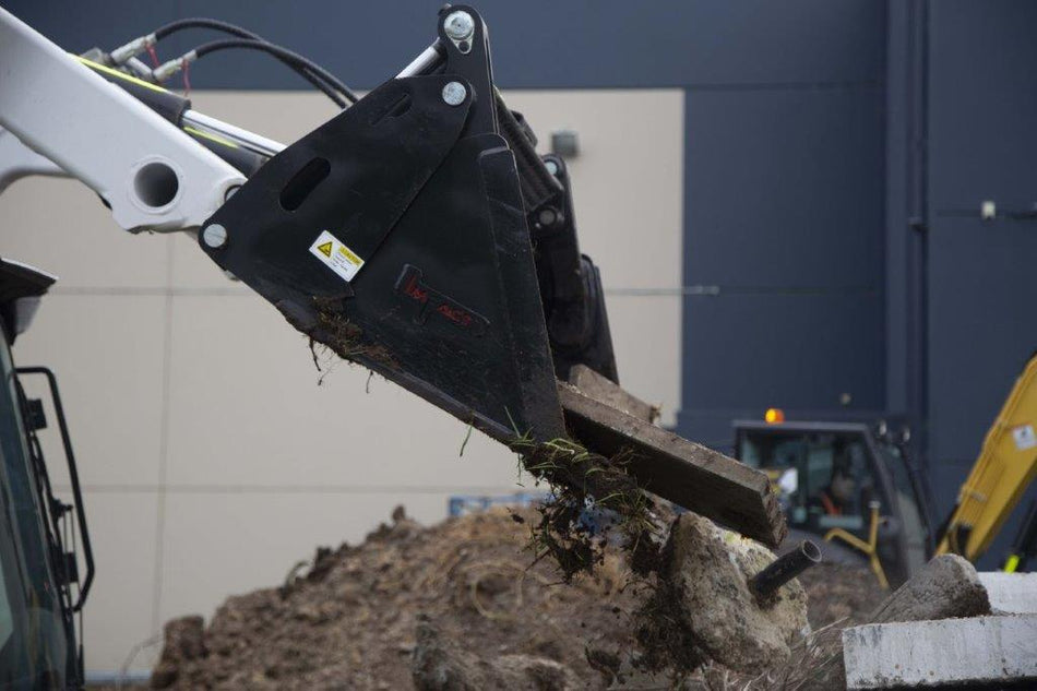 Close-up view of an Impact 4 in 1 bucket attachment on a track loader/skid steer, highlighting the heavy-duty construction and branding, ideal for various excavation and material handling tasks in construction
