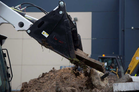 Track loader / skid steer equipped with a 4 in 1 bucket attachment, clearing brush and debris on a construction site, demonstrating versatility and power for heavy-duty tasks. Ideal for various excavation and earthmoving applications