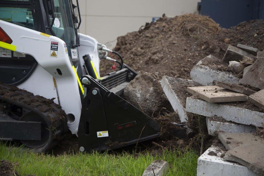 Track loader / skid steer equipped with a 4 in 1 bucket attachment, clearing brush and debris on a construction site, demonstrating versatility and power for heavy-duty tasks. Ideal for various excavation and earthmoving applications