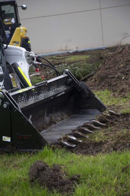 Track loader / skid steer equipped with a 4 in 1 bucket attachment, clearing brush and debris on a construction site, demonstrating versatility and power for heavy-duty tasks. Ideal for various excavation and earthmoving applications