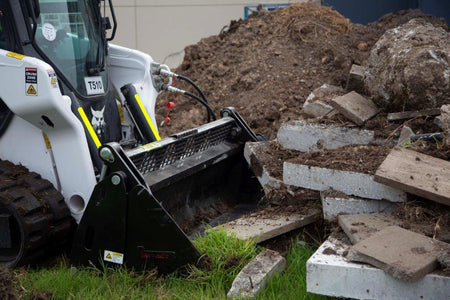 Track loader / skid steer equipped with a 4 in 1 bucket attachment, clearing brush and debris on a construction site, demonstrating versatility and power for heavy-duty tasks. Ideal for various excavation and earthmoving applications.