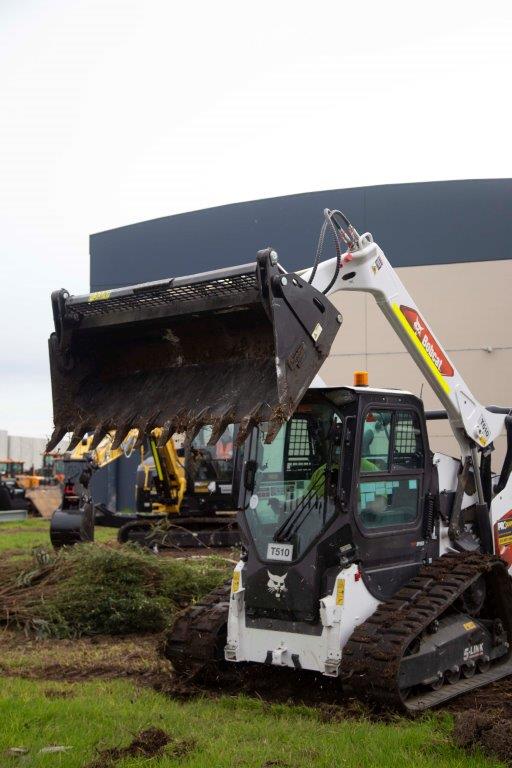 Track loader / skid steer equipped with a 4 in 1 bucket attachment, clearing brush and debris on a construction site, demonstrating versatility and power for heavy-duty tasks. Ideal for various excavation and earthmoving applications