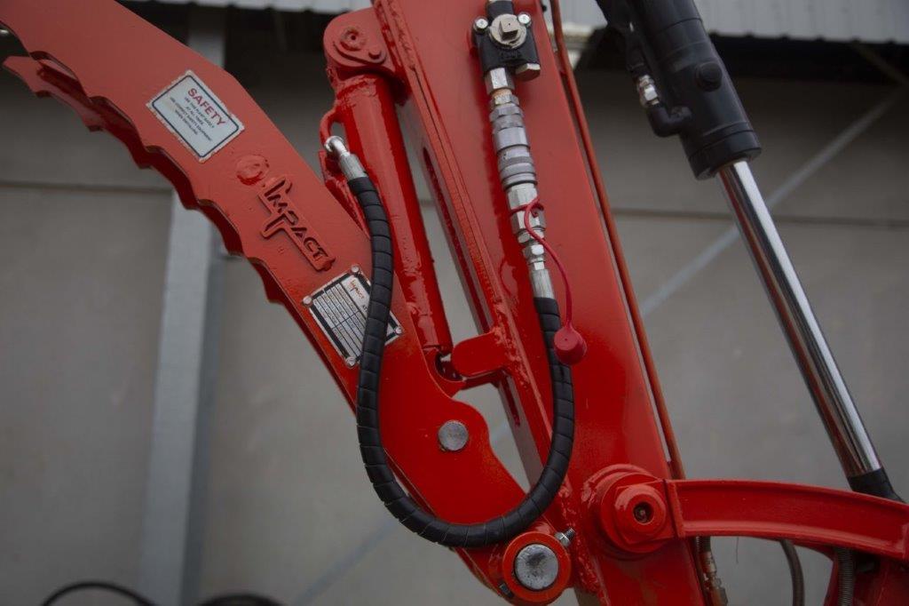 Close-up of an Impact Attachments hydraulic thumb in bright red, mounted on an excavator arm. The hydraulic thumb features a serrated edge designed for gripping and handling materials efficiently. The attachment is equipped with high-quality hydraulic fittings and hoses for optimal performance. Ideal for excavation and material handling tasks, this heavy-duty attachment showcases the durability and precision engineering of Impact Attachments.