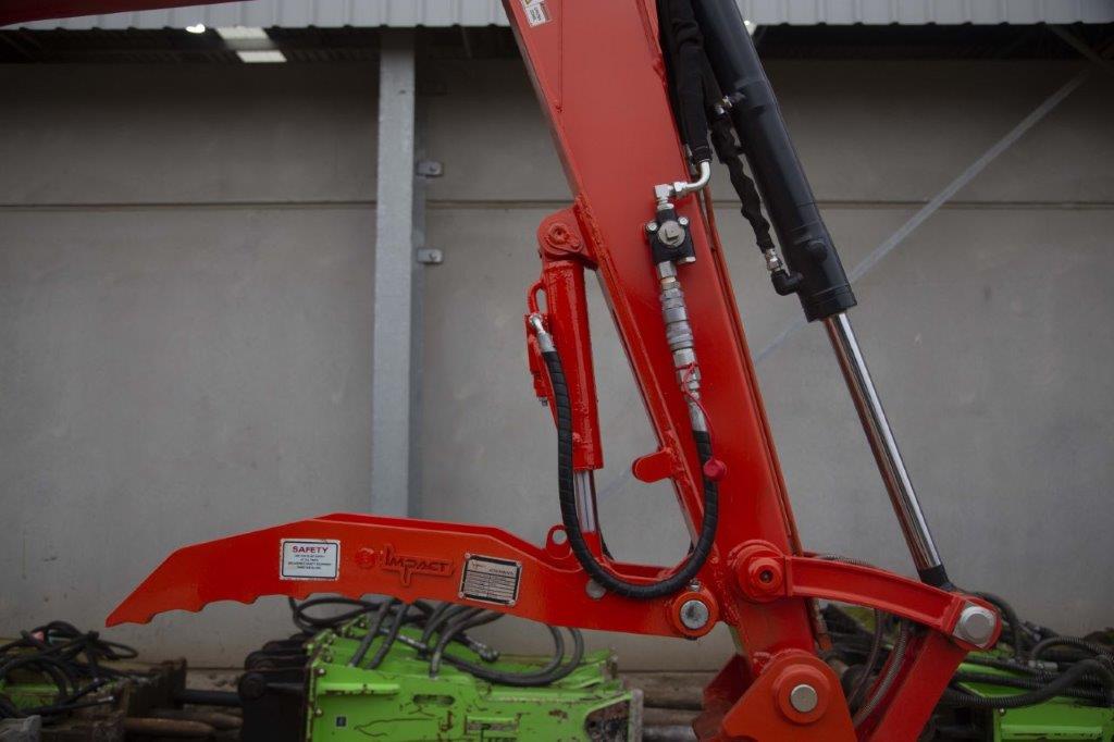 Close-up of an Impact Attachments hydraulic thumb in bright red, mounted on an excavator arm. The hydraulic thumb features a serrated edge designed for gripping and handling materials efficiently. The attachment is equipped with high-quality hydraulic fittings and hoses for optimal performance. Ideal for excavation and material handling tasks, this heavy-duty attachment showcases the durability and precision engineering of Impact Attachments.