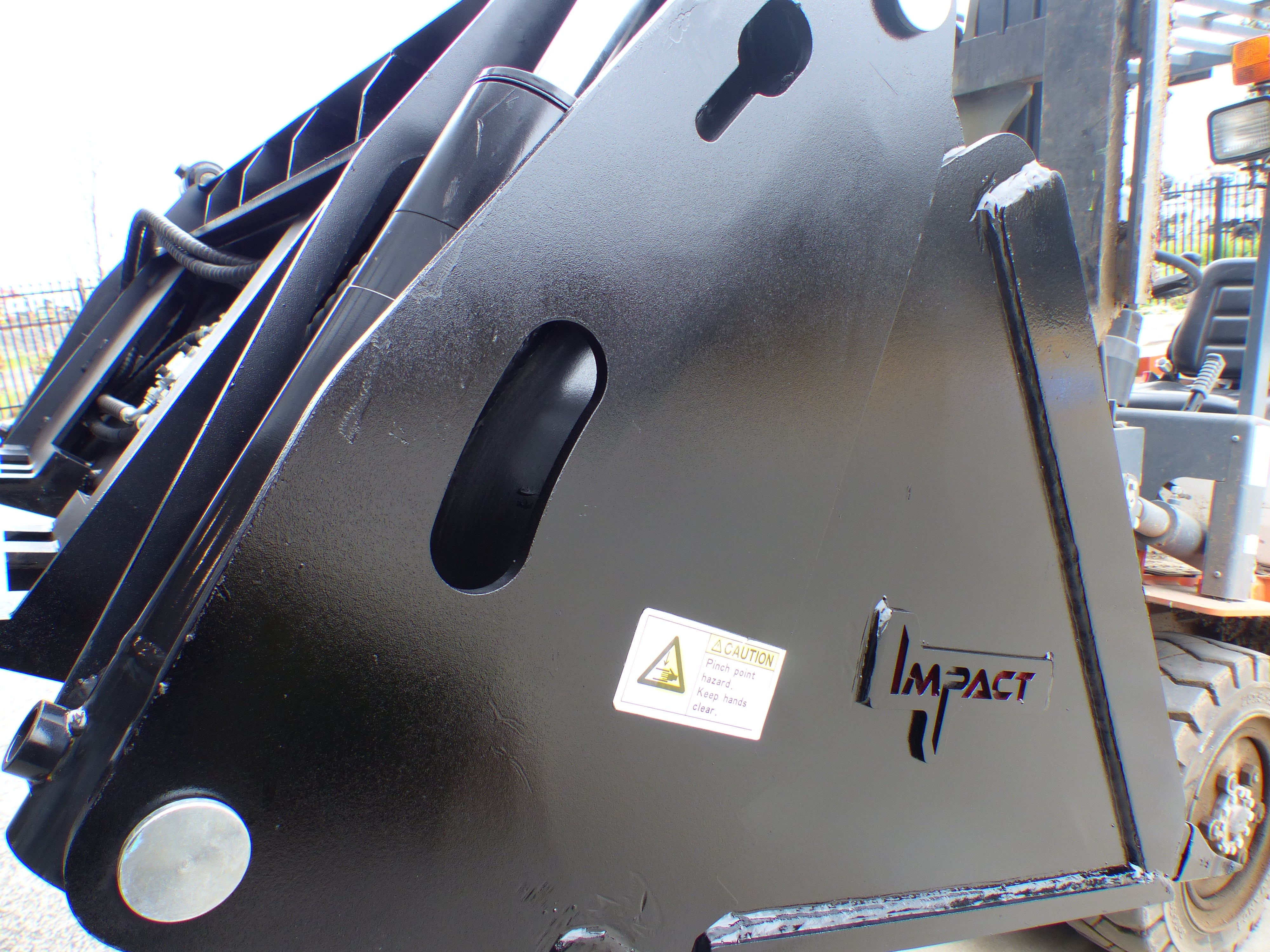 Close-up view of an Impact 4 in 1 bucket attachment on a track loader/skid steer, highlighting the heavy-duty construction and branding, ideal for various excavation and material handling tasks in construction
