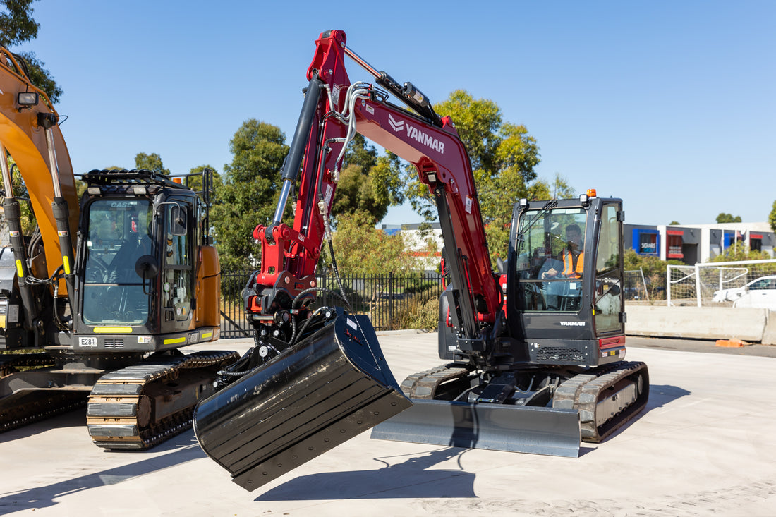 Yanmar excavator equipped with a hydraulic tilt bucket, showcasing its versatile movement. The excavator is set up on a concrete surface, with another CASE excavator visible in the background. Ideal for construction projects requiring precise grading and digging