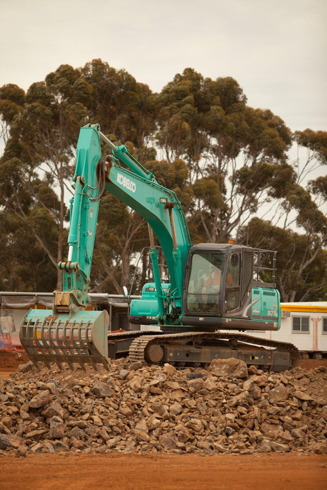 Kobelco excavator equipped with an Impact Attachments sieve bucket, sorting and handling rocks at a construction site.