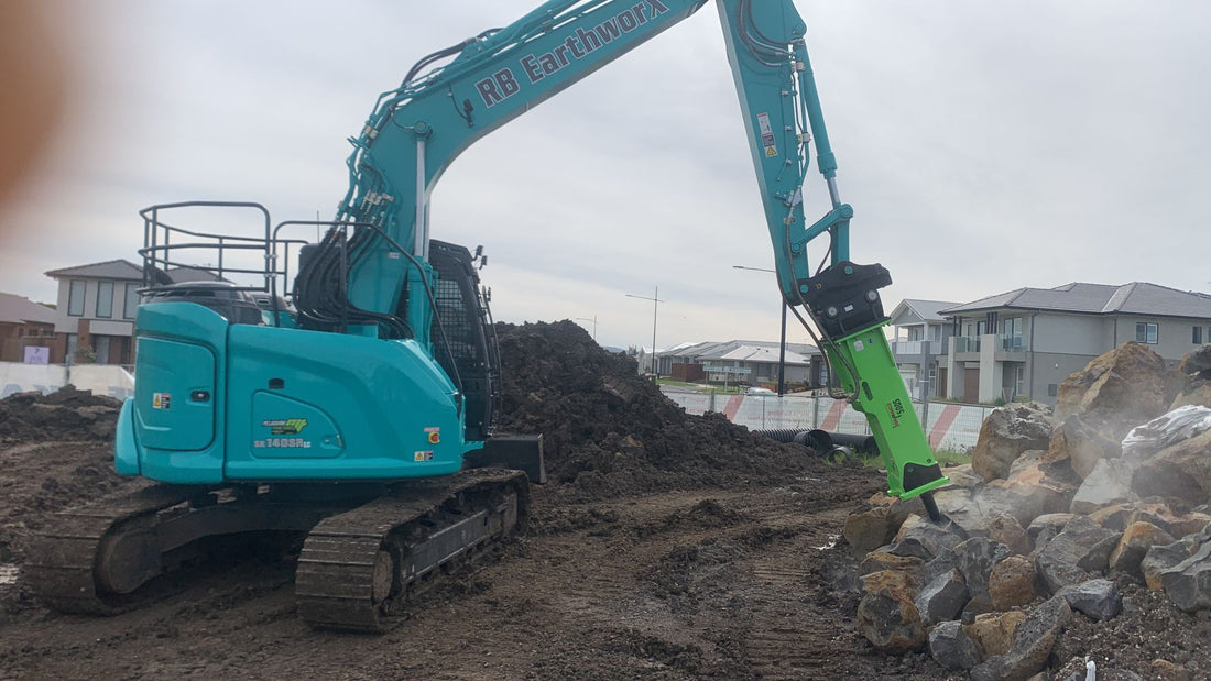 Kobelco SK140SR excavator with Impact Attachments hydraulic breaker demolishing rocks on a construction site, demonstrating heavy-duty performance